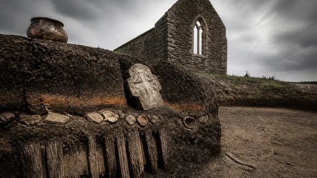 Man in winter hat examining an ancient artifact beside moss-covered stones at Chapel Head archaeological dig site in…