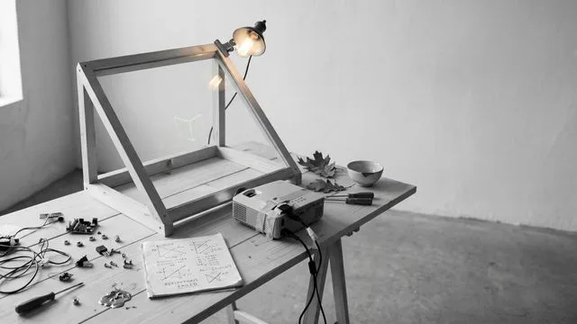 A wooden desk with a green cutting mat displays a holographic screen showing focus timer, weather, CPU/RAM stats, and…