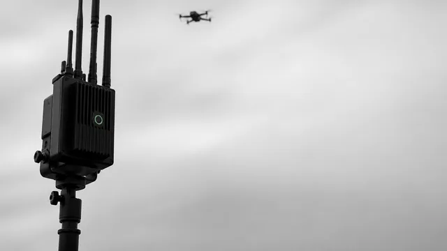 Person holding RF spectrum analyzer displaying signal readings next to dual monitors showing drone video feed from vehicle…
