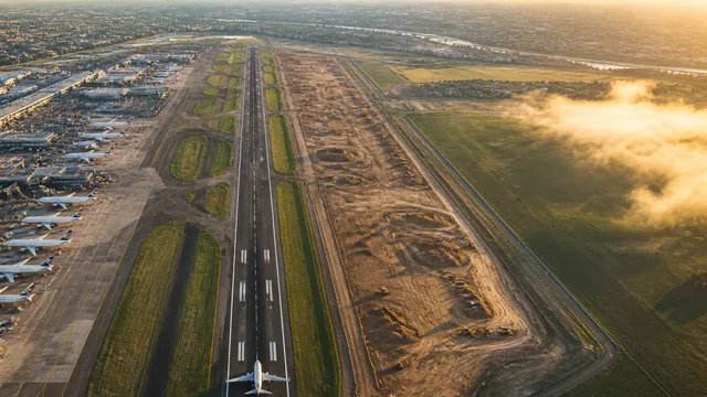 Aerial view of a large airport highlighted in gold overlaid on suburban landscape with text "IN THE WRONG PLACE