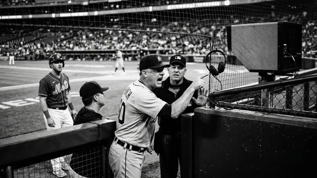 Detroit Tigers manager in navy cap and yellow sunglasses adjusting his hat in frustration at the dugout with "AWFUL REPLAY"…